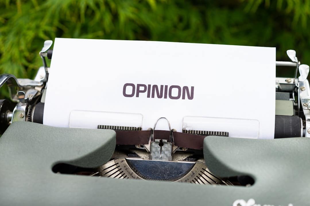 Vintage typewriter with a sheet reading OPINION outdoors on green grass.