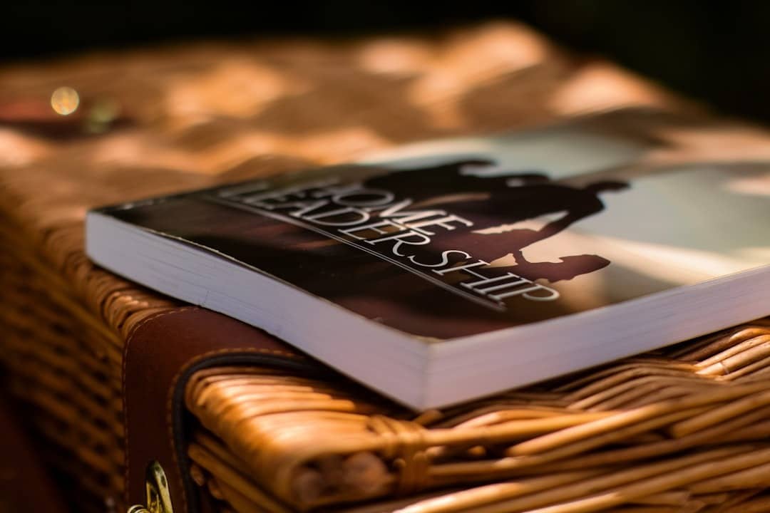 Close-up of a paperback book with dark cover and silhouettes, resting on a woven wicker surface or trunk.
