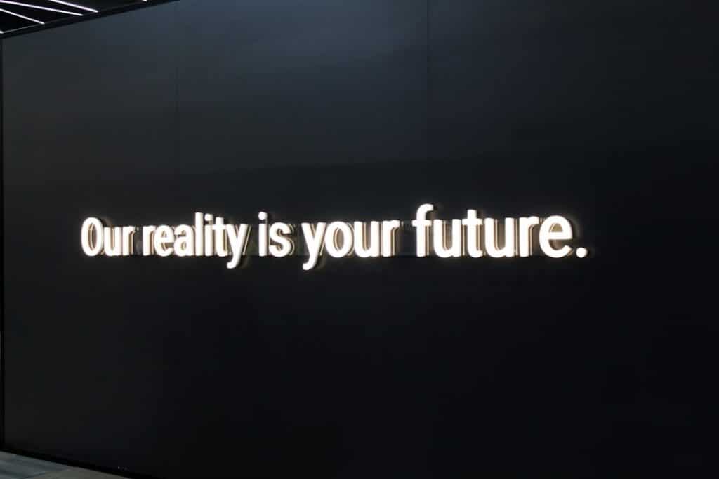 Black wall with bright white illuminated text:'Our reality is your future.'