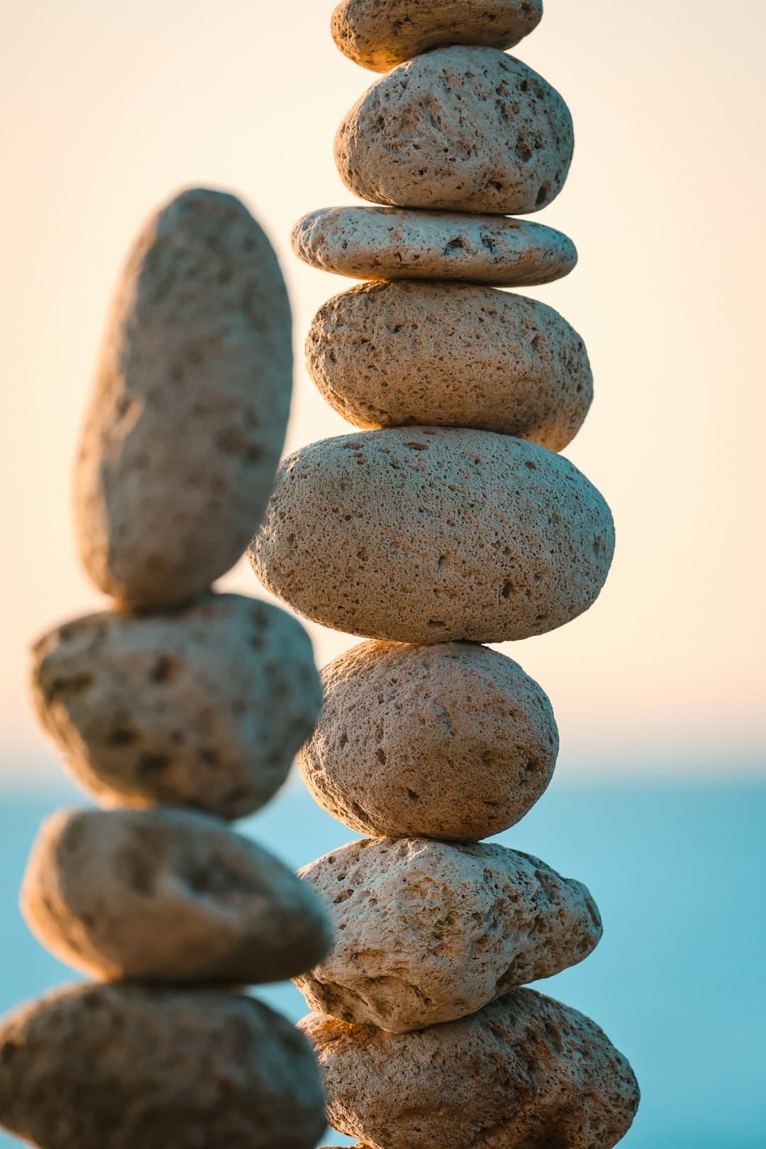 Stacked smooth stones balanced into a vertical tower at the beach during sunset the calm sea in the background