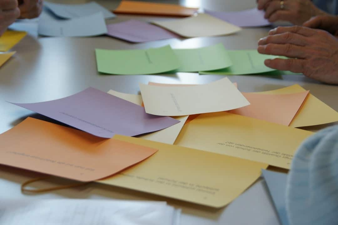 Hands of several people around a table organizing pastel-colored cards/envelopes in a group workshop setting.