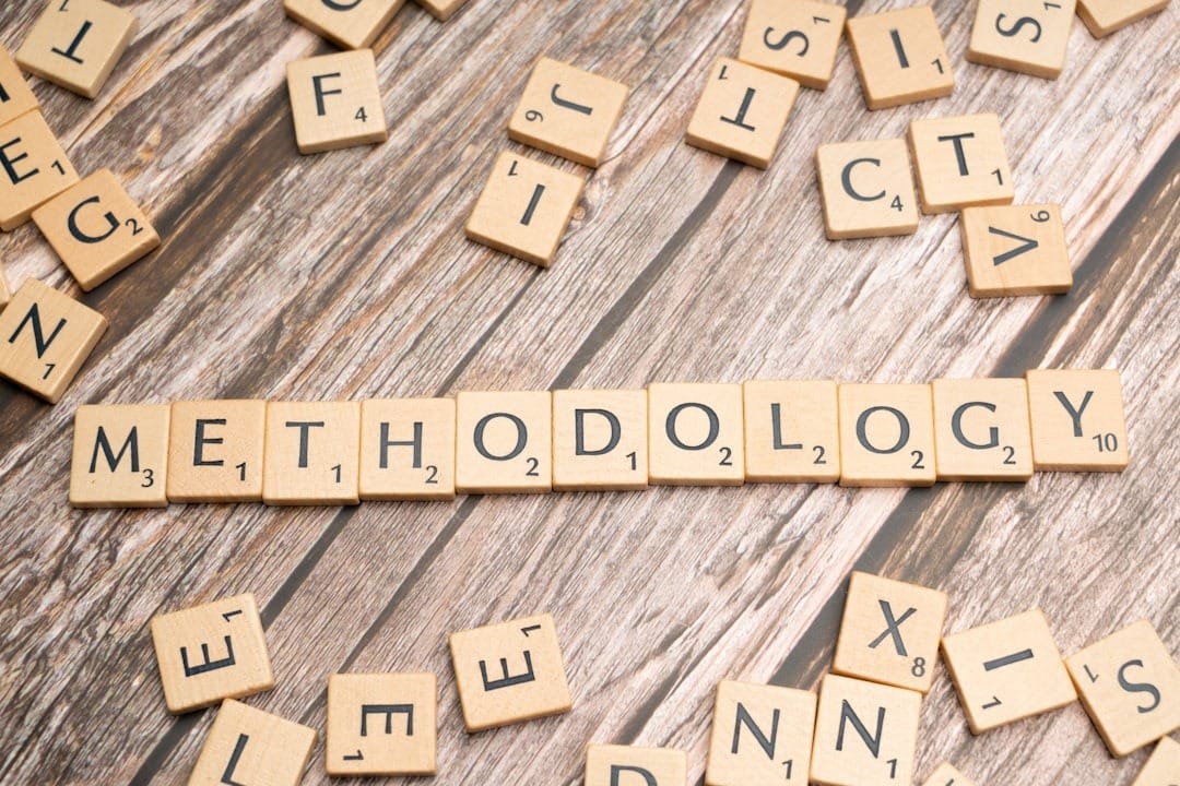 Scrabble tiles spell 'METHODOLOGY' on a wooden table with scattered letters around it.
