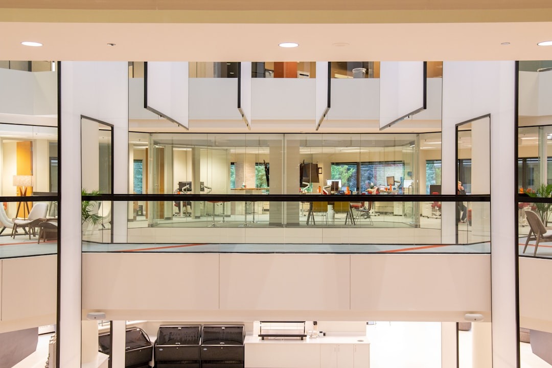 Open, modern office atrium with glass-walled meeting rooms on the upper level and visible seating areas.",