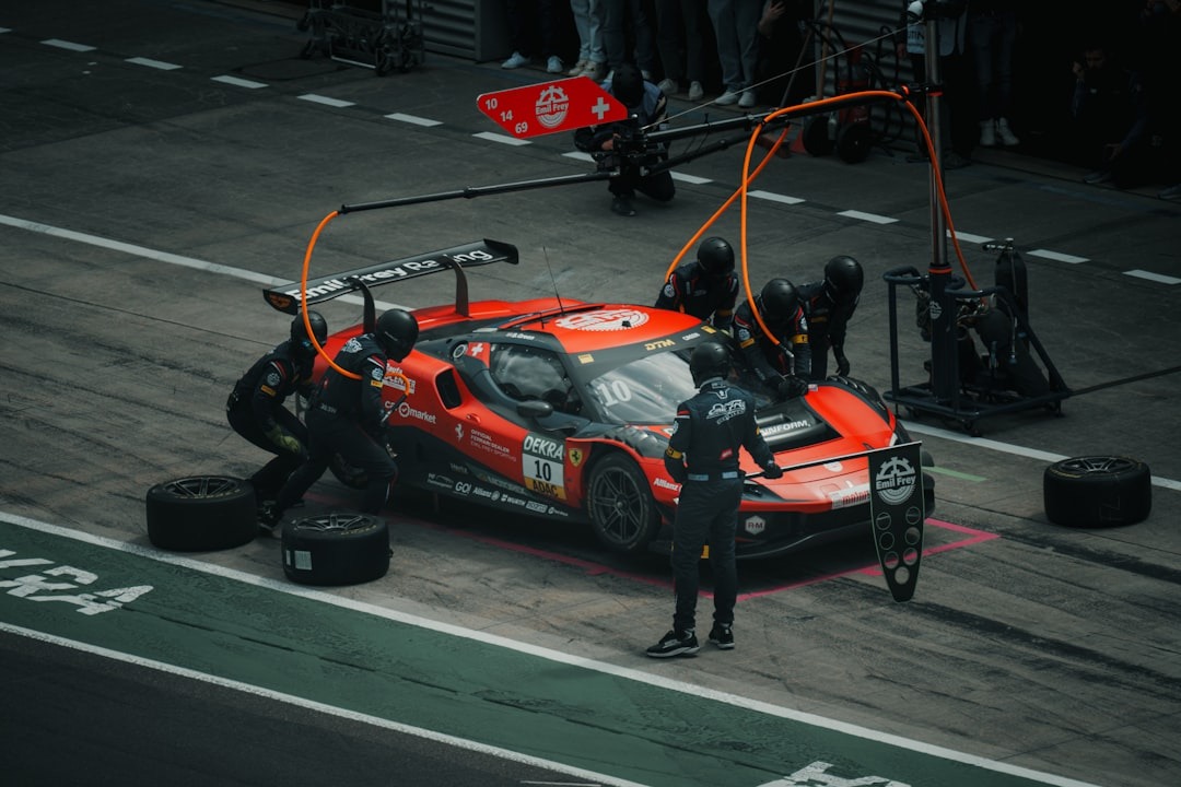 Red Ferrari race car in a pit stop with multiple crew members changing tires nearby.