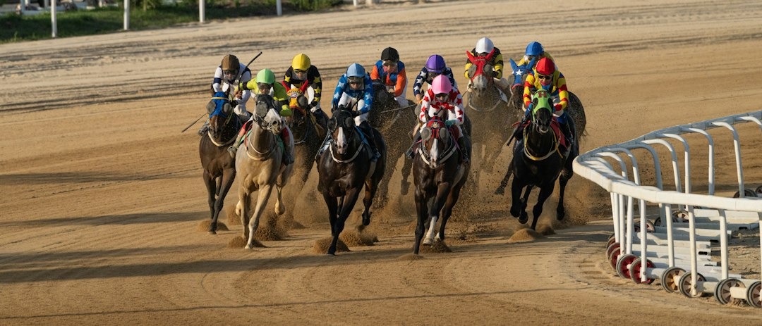 Group of jockeys racing on a dirt track, colorful silks flying as horses round a bend near the rail.