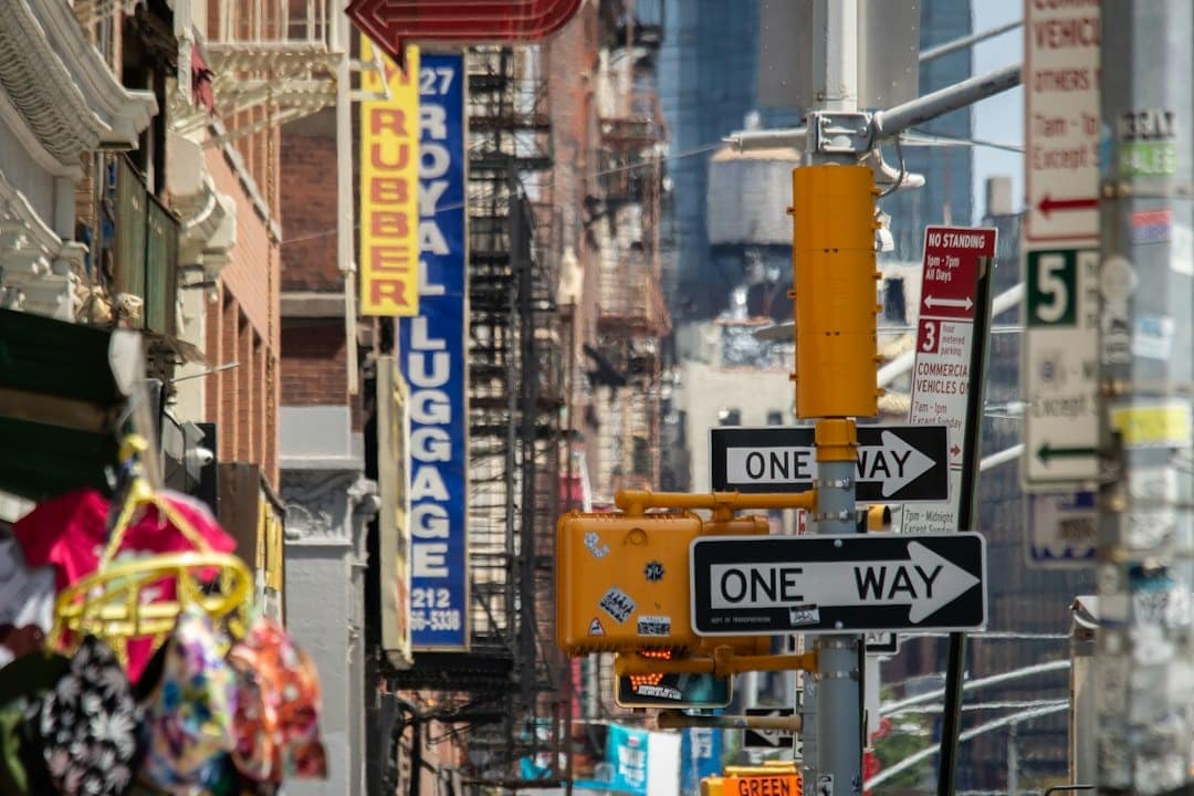 Busy urban street intersection with one-way signs, a yellow traffic signal housing, and storefronts on both sides of the street.