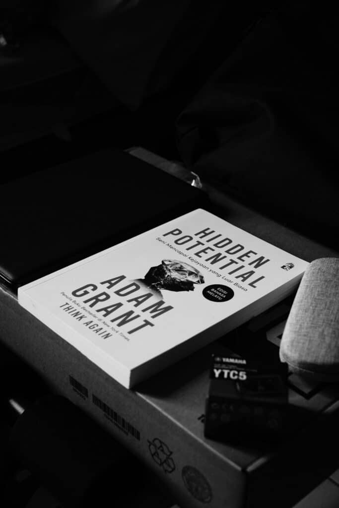 Black-and-white close-up of a book cover showing'Hidden Potential' and 'Adam Grant Think Again' resting on a cardboard box